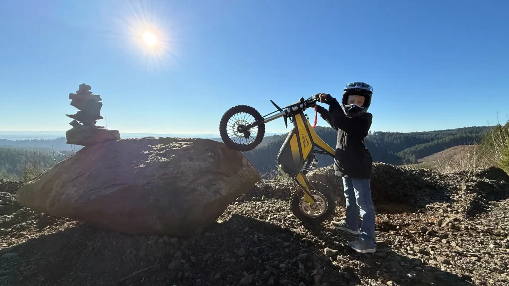 Electric dirt bike trial riding on rocky terrain with young rider wearing helmet